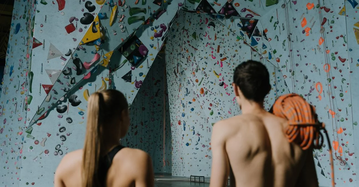 Deux athlètes se préparant à grimper un mur de bloc coloré en salle avec des équipements de sécurité.