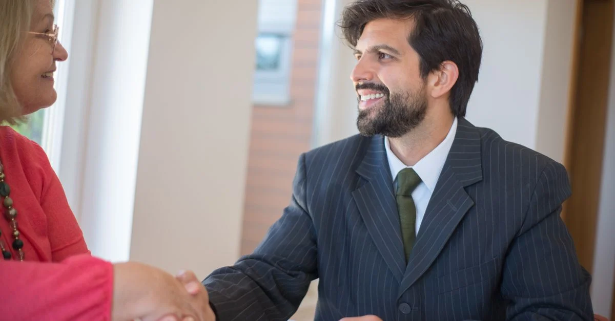 Agent immobilier professionnel scellant un accord avec un client senior à l'intérieur par une poignée de main.