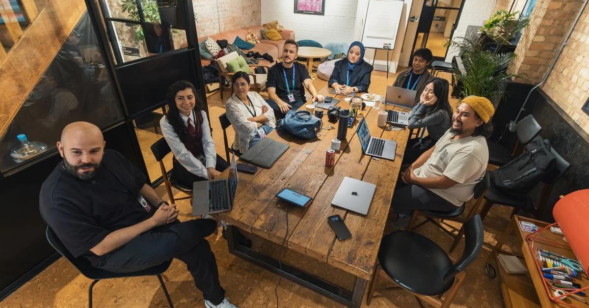Groupe de collègues rassemblés autour d'une table dans un cadre de bureau moderne, collaborant sur des ordinateurs portables.