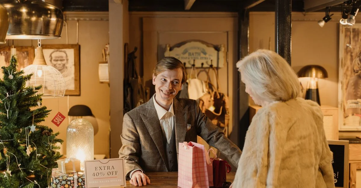 Un commerçant joyeux aide un client lors d'un événement de vente festive dans un cadre de magasin confortable.